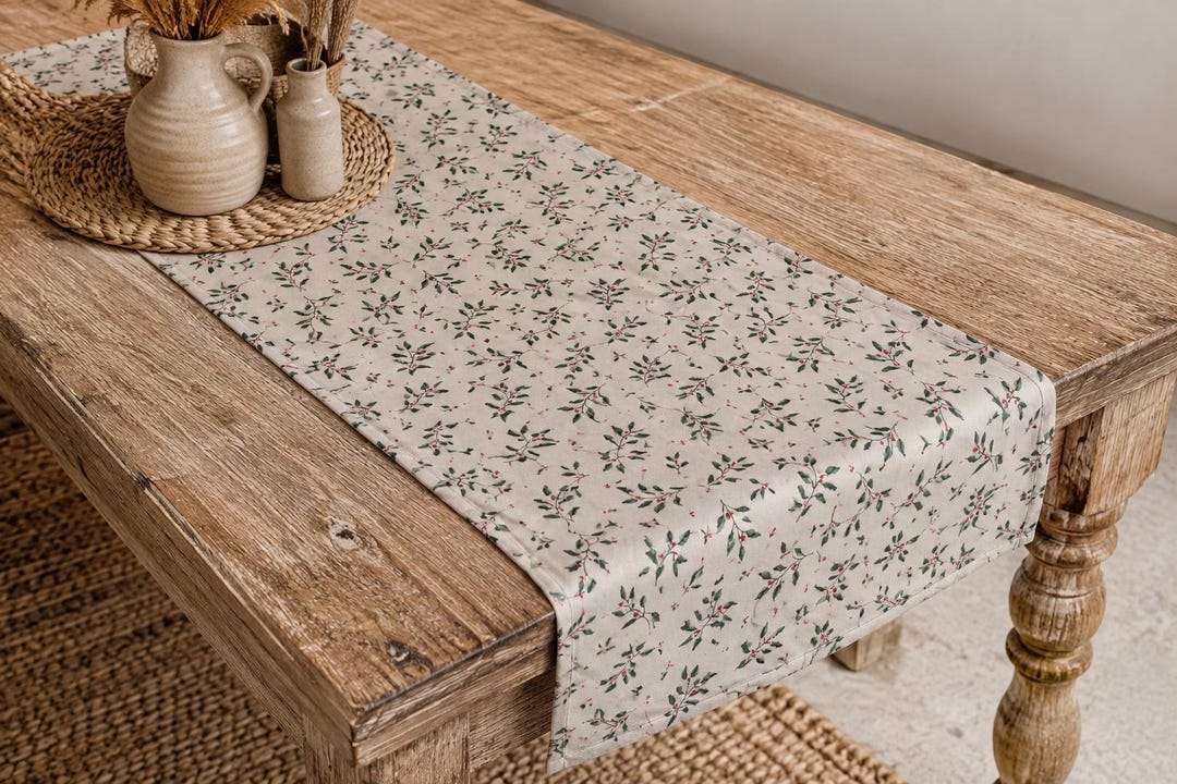 Tischläufer mit grünen Blättern und roten Beeren auf hellbeigem Grund auf einem Holztisch